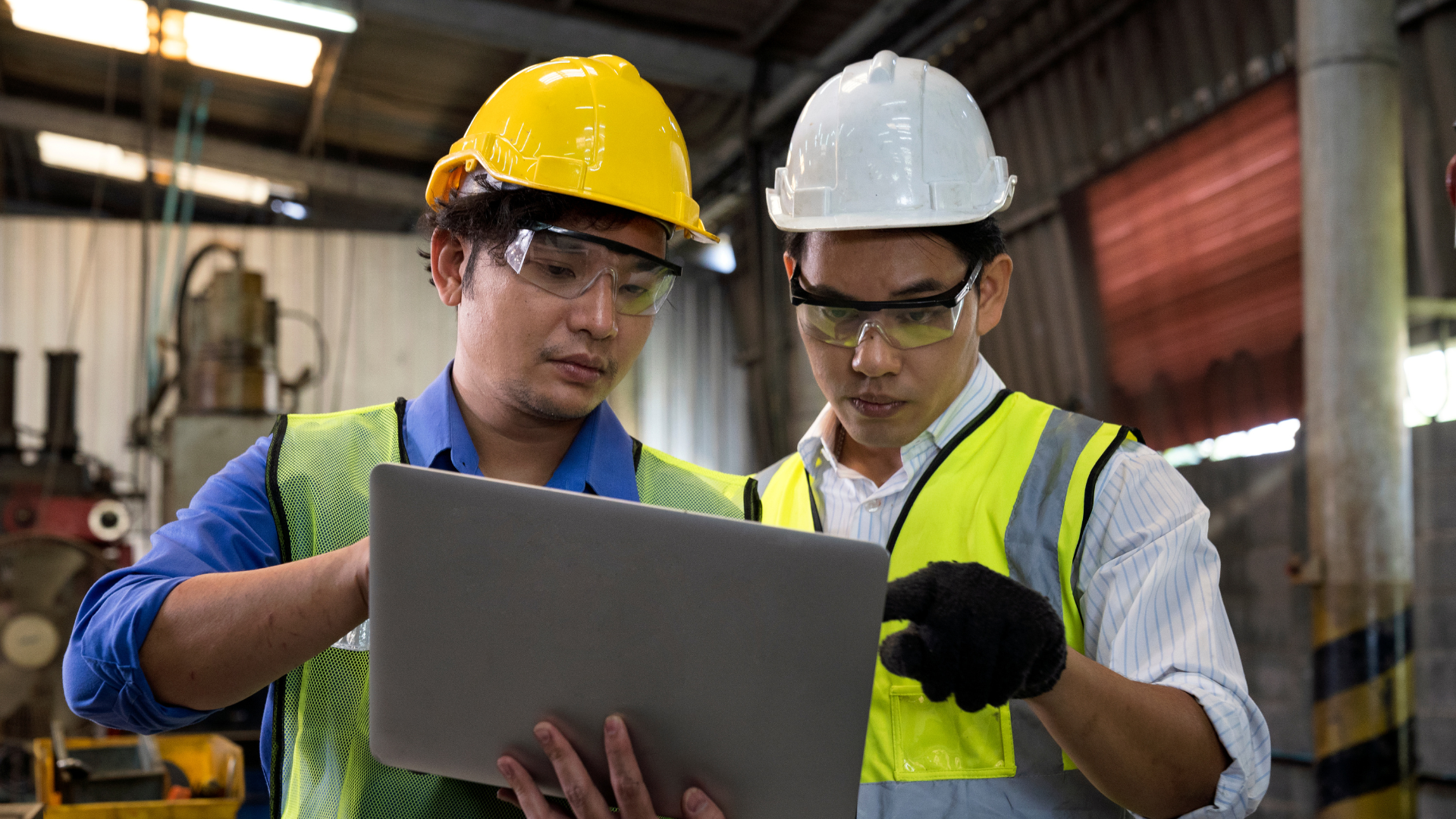 two men with laptop and industrial control machine in background