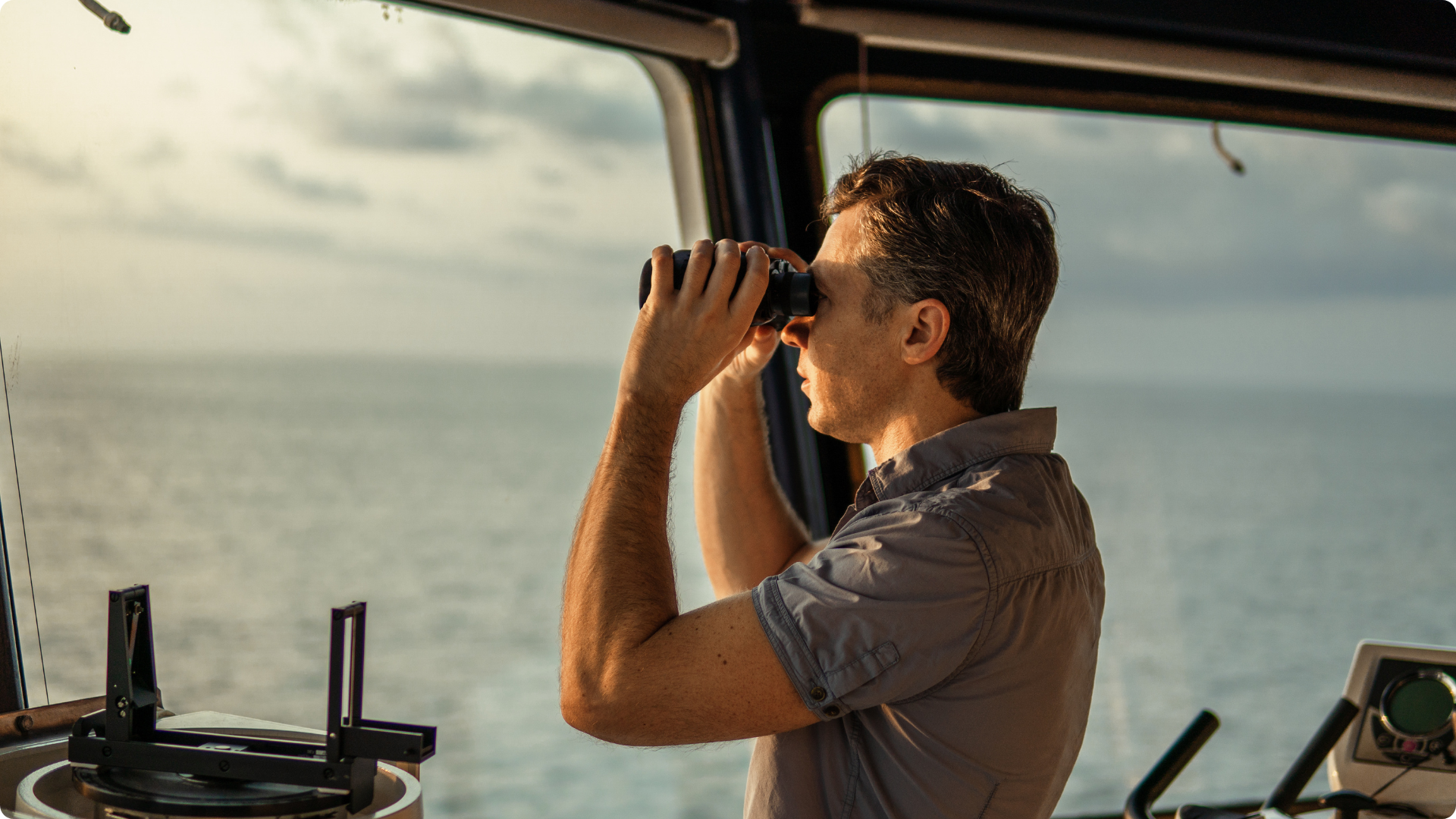 man on ship looking out with binoculars