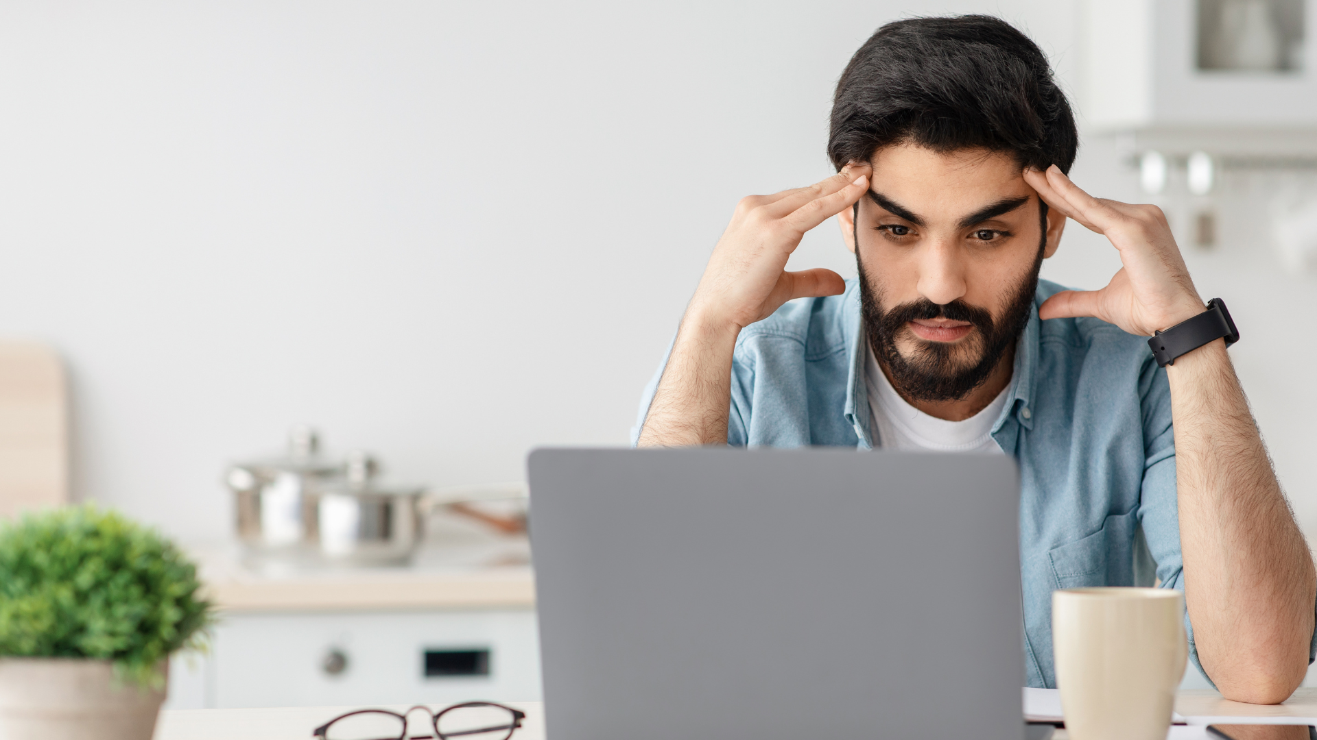 man holding his head while looking at laptop